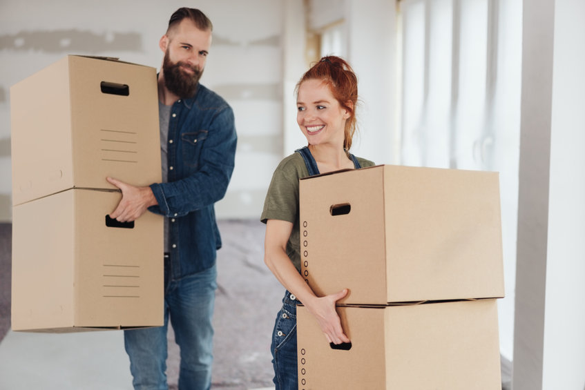 a man and woman carrying cardboard boxes in an empty room