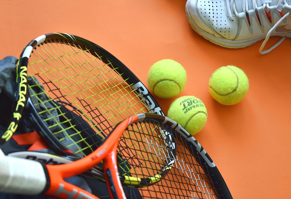 tennis racket, tennis balls and tennis shoes on an orange surface