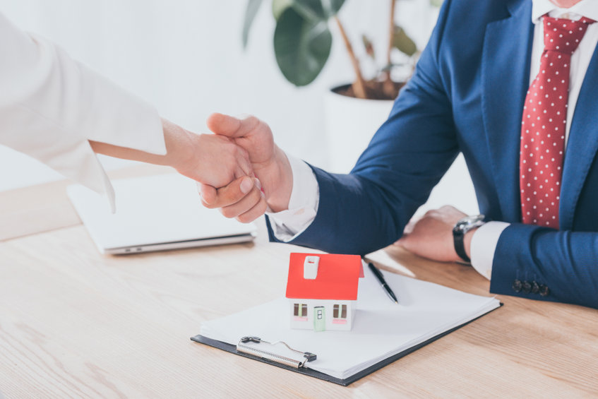 a man and woman shaking hands over a house model