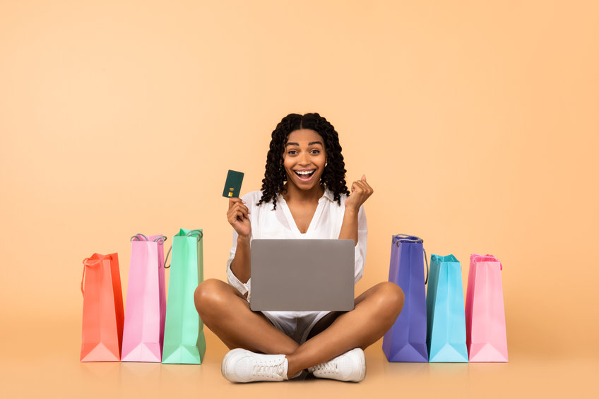 happy african american woman with laptop and credit card on orange background