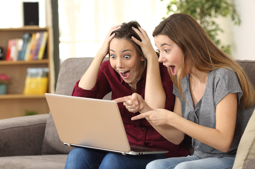two women sitting on a couch with a laptop