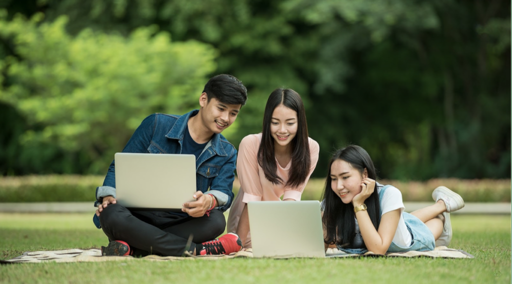 three young asian students using laptops in the park