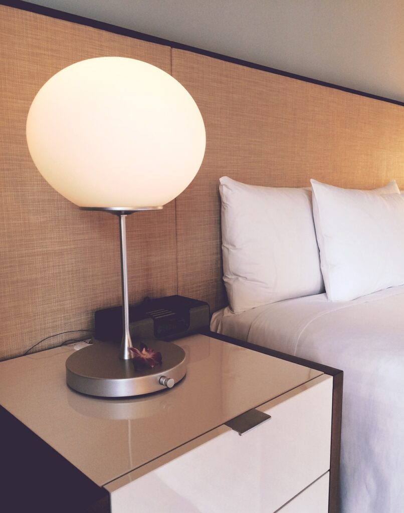 Une lampe sphérique allumée sur une table de chevet à côté d'un lit avec des oreillers blancs.