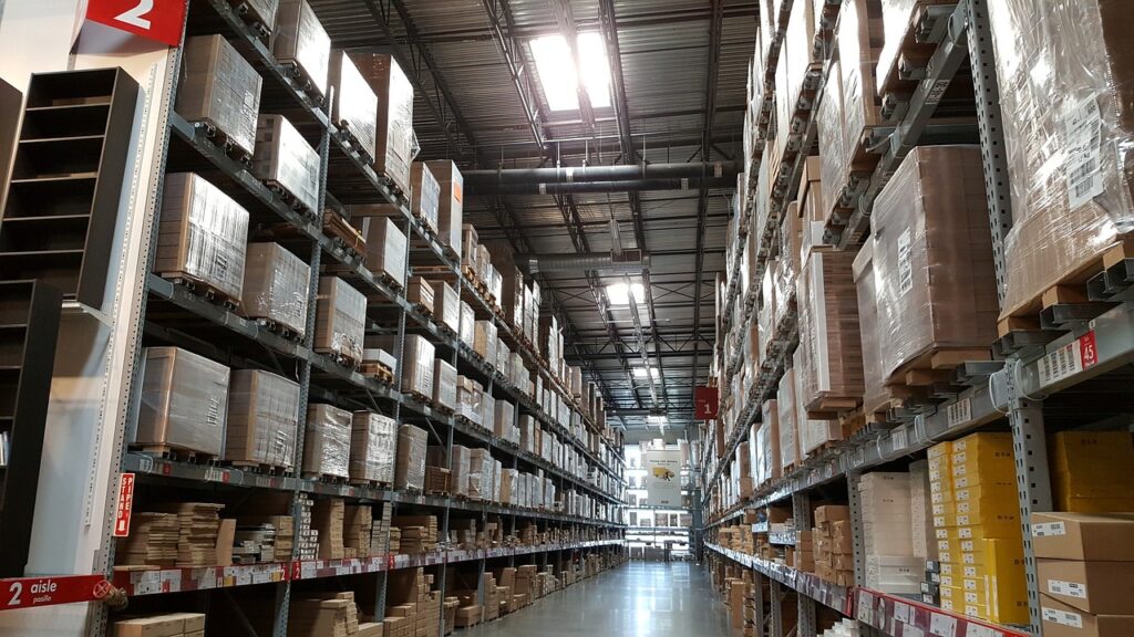 Un grand entrepôt avec des étagères hautes remplies de boîtes et un couloir central.