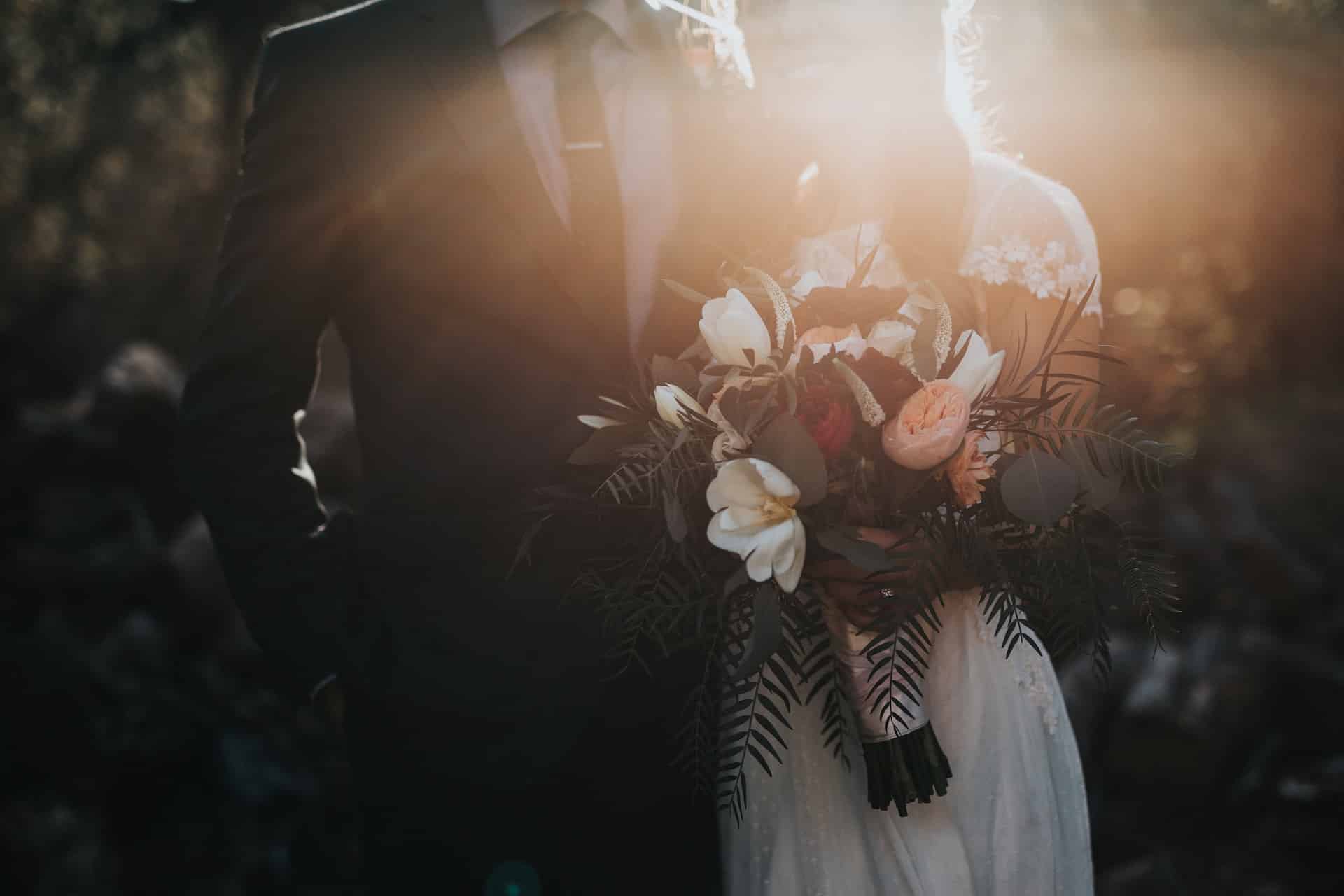 Un couple de mariés tenant un bouquet avec un éclairage en contre-jour dans un cadre naturel.