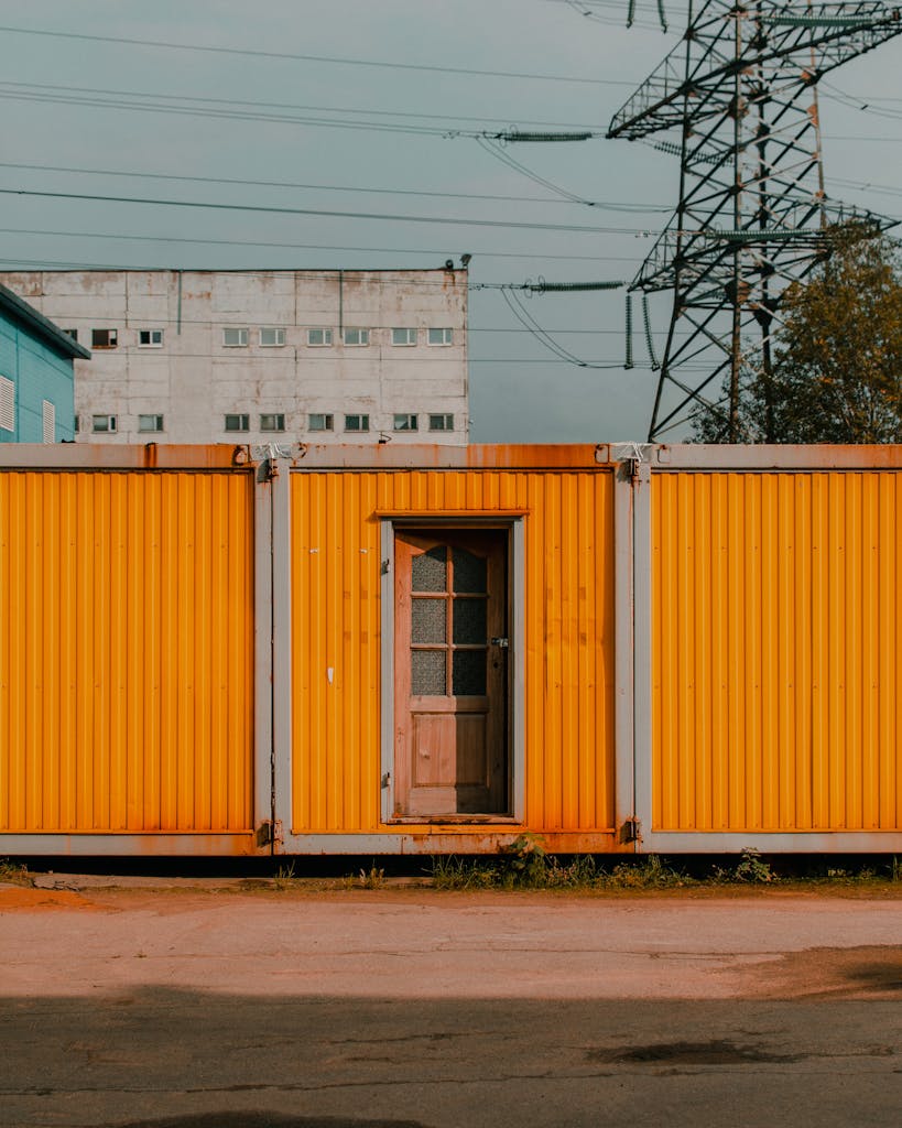 A vibrant yellow container featuring a rustic wooden door, set outdoors with an industrial backdrop.