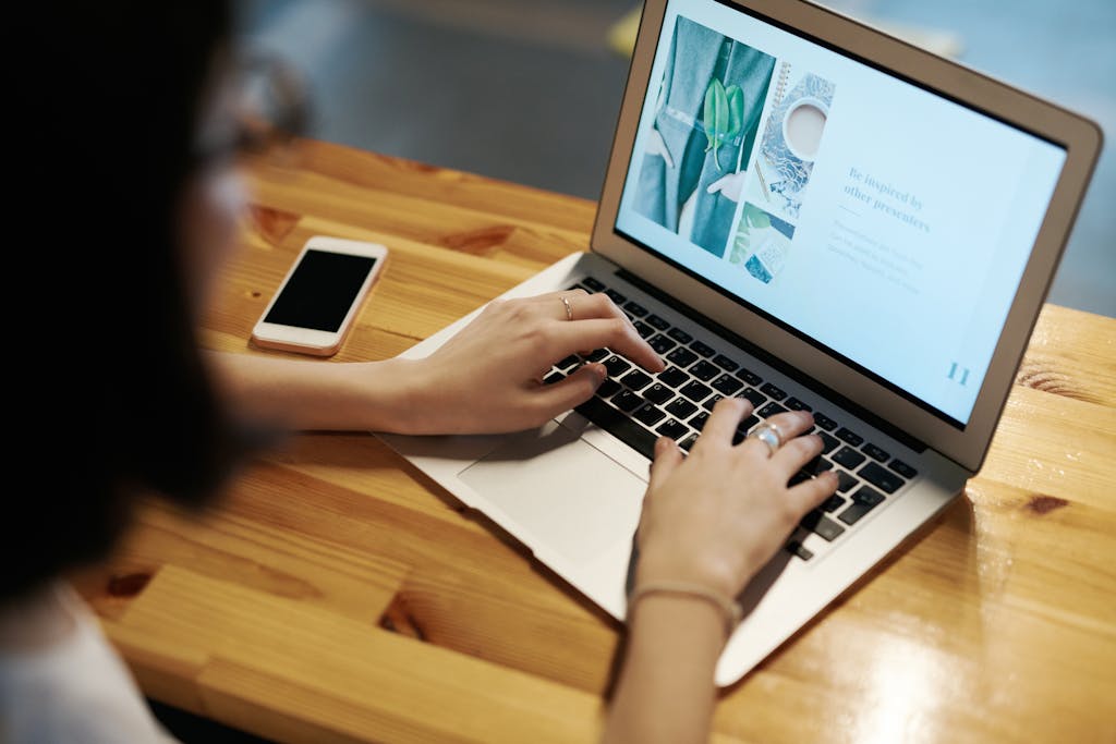 Person typing on a laptop at a wooden table with a smartphone nearby, illustrating remote work.