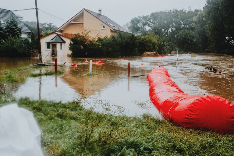 Flooded residential area protected by red flood barriers, showing severe weather impact.