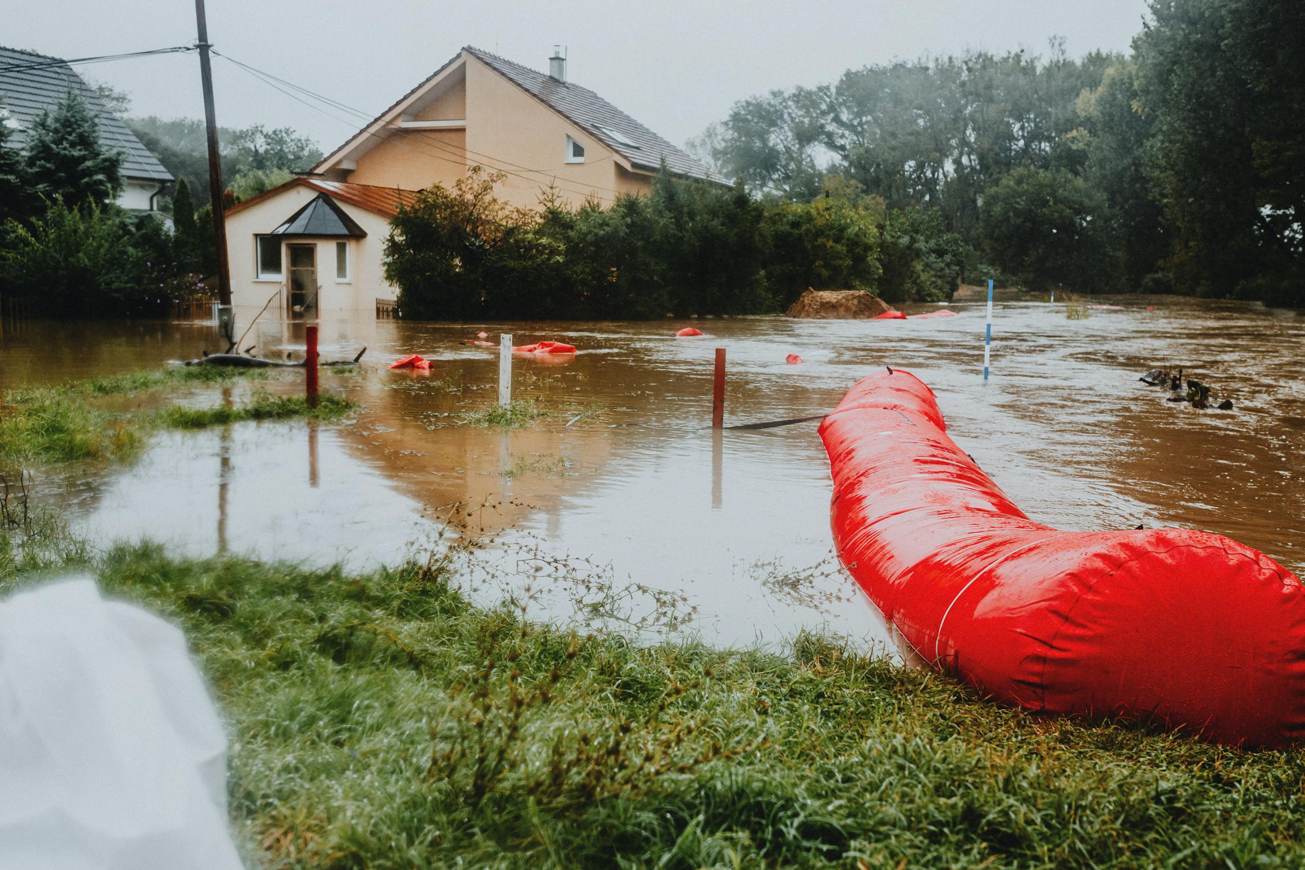 Flooded residential area protected by red flood barriers, showing severe weather impact.