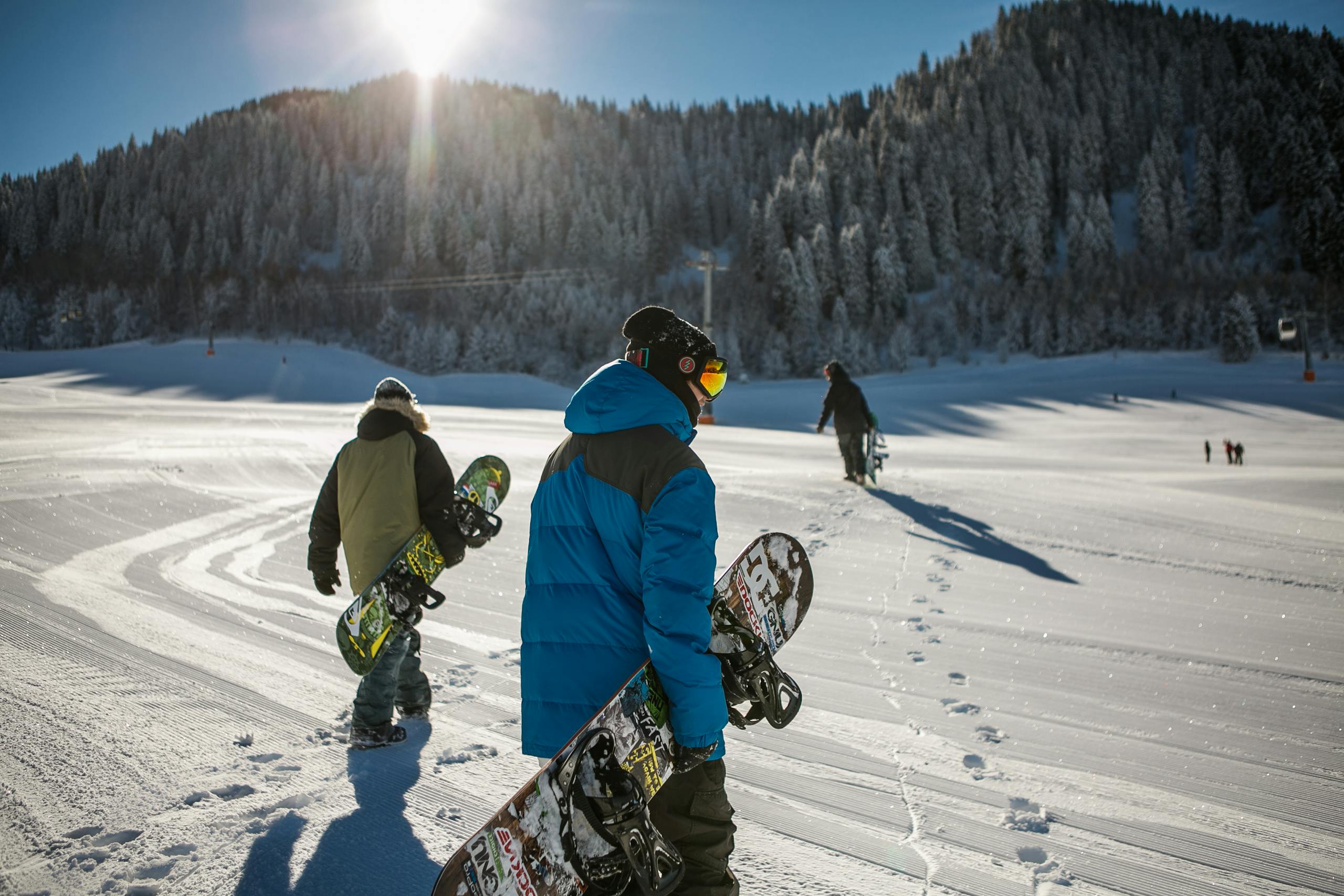 Group of snowboarders walking up a snowy ski slope during a sunny winter day in the mountains.